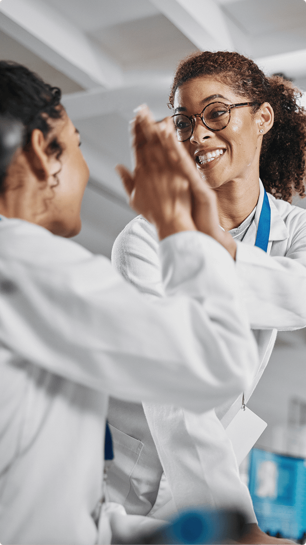Two smiling scientists in lab coats high-five in a laboratory setting, conveying teamwork and success. The atmosphere is joyful and collaborative.