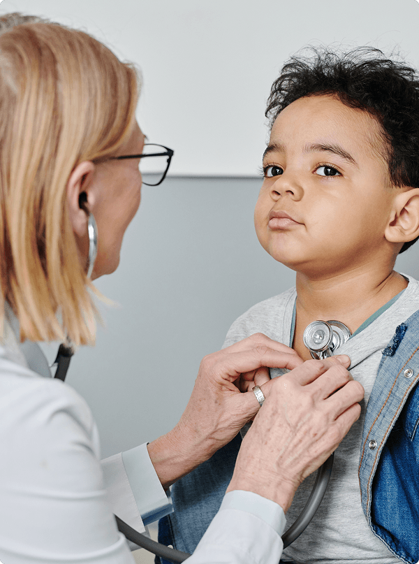 A healthcare professional with a stethoscope examines a serious-looking child. The setting is clinical, conveying careful attention and care.